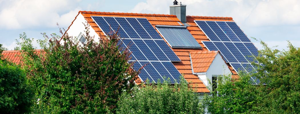 Hausdach mit Solarmodulen und Solarthermie. Davor grüne Bäume